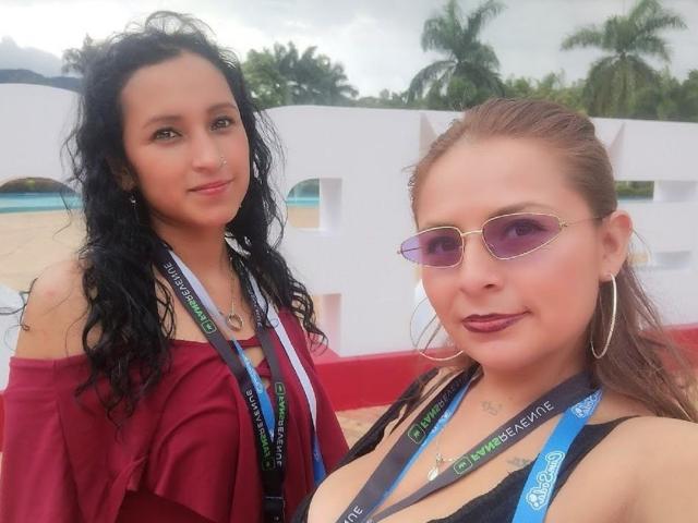 Two XimenaNahomi's with lanyards, one with curly black hair in a red off-shoulder top, the other with brown hair in a black top, wearing pink sunglasses.