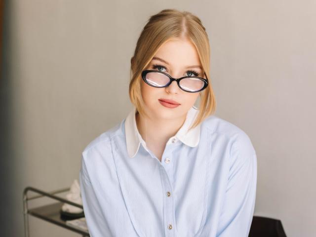 NicoleBrian with blonde hair, blue eyes, and glasses, wearing a light blue shirt with a white collar, has a cute, sexy face and a subtle smile.