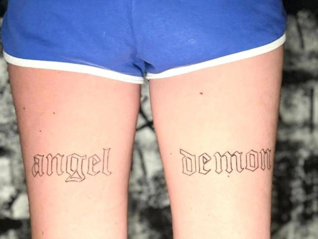 Les jambes de RoxyXXX-hot sont ornées de tatouages représentant un "ange" et un "démon", avec une police gothique noire, sur les cuisses extérieures. Elle porte un short bleu avec une bordure blanche, qui révèle sa peau pâle..