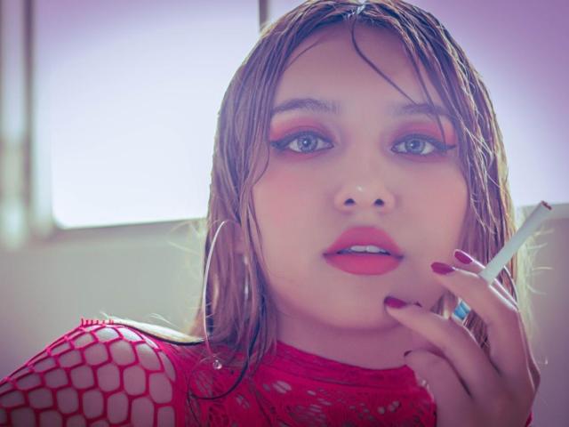 LillyTaylor with wet brown hair, red fishnet top, red eyeshadow, red lipstick, holding a cigarette, red nails, looking at camera, soft purple light, subtle makeup, cute.