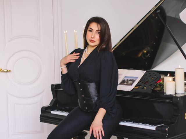 OliviaCluff, with dark brown hair, wearing black dress, corset, and pearl necklace, sitting on piano, hand on chest, candles in background, piano open, white door, sexy.