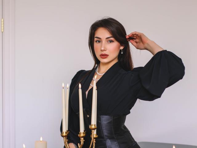 OliviaCluff with dark hair, wearing a black blouse with puffy sleeves, pearl necklace, and black leather corset, holding a gold candelabra with lit candles, right hand in hair.