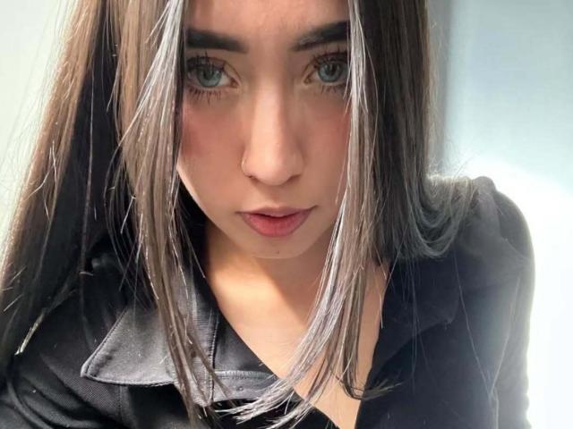 BabiMoonn with long brown hair, blue eyes, and a nose ring, wearing a black shirt, looking directly at the camera with a serious expression.