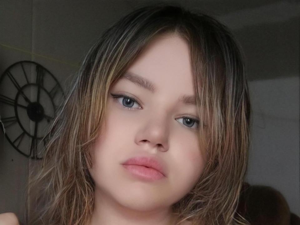 PlusSizeHt with blonde, wet-looking hair, blue eyes, and pink lips, looking slightly bored, has subtle black eyeliner, and a fair skin tone, showing a neutral expression.