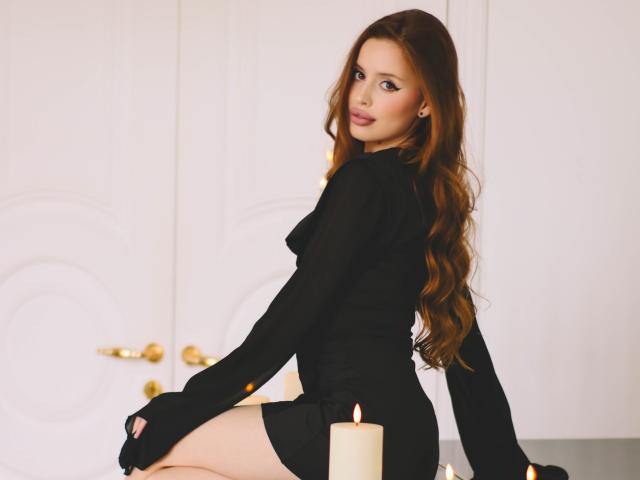 CherylFoxy with long brown hair, black dress, sitting on a table, candle in front, looking back, butt visible, white doors in background, soft lighting, slight smile.