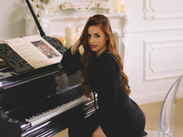 CherylFoxy with long red hair, black dress, and large ass, sitting at a glossy black piano, hand on her head, looking over her shoulder with a sexy smile.