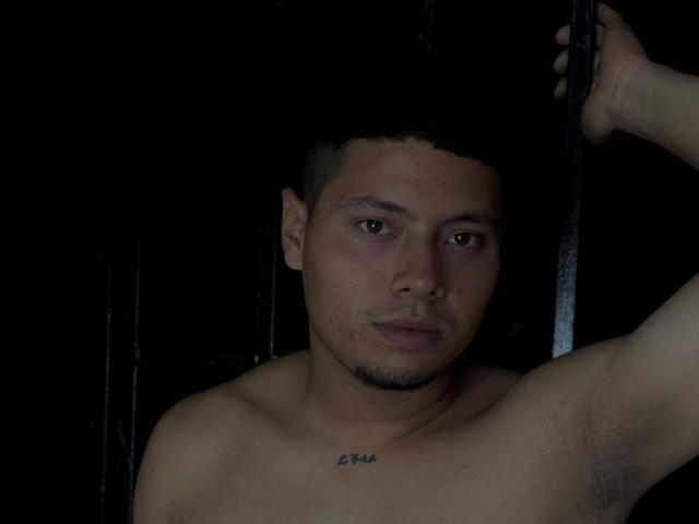 StevenClain has short black hair, brown eyes, and a tattoo on his chest. He's shirtless with a slight beard, holding a black pole, and has armpit hair.