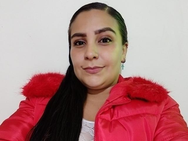 SalmaLopez has medium brown skin, long black hair in a ponytail, wearing a red jacket with fur trim, and a white lace top, smiling softly.
