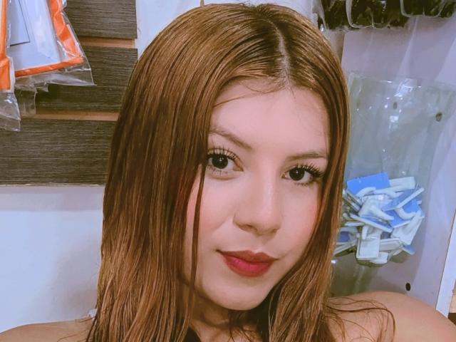 AbejitaHot has long brown hair, light skin, and is smiling with red lipstick. She has big eyes and is looking at the camera. Her tits are not visible.
