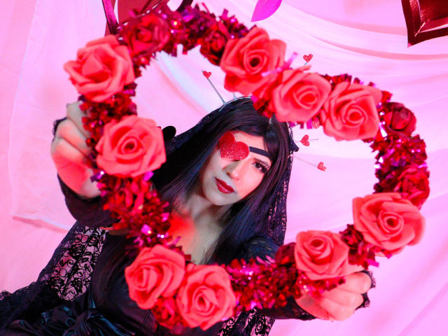 EvangelineAx with black hair, red heart-shaped eyepatch, and black lace dress, holding a red rose wreath, has pink and purple lighting on her face and chest.