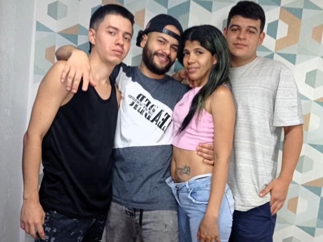 MarcelaAndBoysSexyGroup: four people standing, Marcela with green hair, small tits, pink crop top, jeans, next to three guys, bearded guy in gray shirt, black cap, others in tank tops.