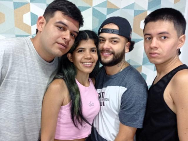 MarcelaAndBoysSexyGroup: four people, Marcela with green hair, pink top, small tits, next to three boys, Marcela's arm around them, gray shirt, black tank top, baseball cap.