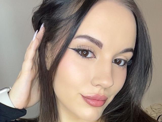 LaylaBusty69 has pale skin, dark brown hair, and is showing off her flirty eyeliner with long, pointed lashes. She's pouting with pink lips and touching her hair.