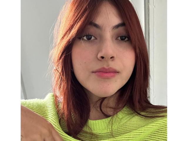 SpencerLe, avec ses cheveux roux, son pull vert et son maquillage discret, a de petites seins et un joli visage. Elle regarde directement l'appareil photo avec un léger sourire confiant..