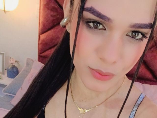 AliceCoolenk has long black hair, purple eyebrows, pink lipstick, and a gold necklace. She's wearing a black top with a pink blush on her cheeks.