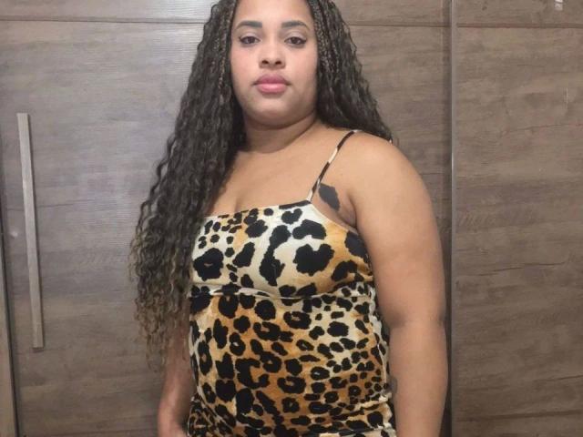 SuelenBarbar4-hot with long curly brown hair, brown skin, wearing a leopard print dress, standing in front of wooden cabinets, looking at the camera with pink lipstick.