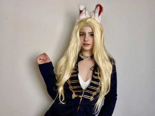 MarriAnni with long blonde wig, white rabbit ears, blue eyes, black jacket with gold buttons, white shirt, choker, standing, right fist raised. Boobs visible under jacket.