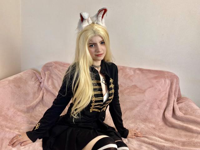 MarriAnni with long blonde hair, white fox ears, black buttoned jacket, black skirt, striped thigh-highs, sitting on pink couch, cute, small tits, fair skin, slight smile.