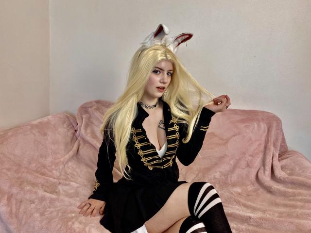 MarriAnni with long blonde hair, white fox ears, black dress with gold trim, exposing her tits, black thigh-highs, sitting on pink sofa, holding her hair.