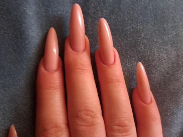 Los dedos de AnnaLuiza, con uñas largas, brillantes y de color piel, apuntan hacia arriba, descansando sobre una superficie oscura y texturizada. No hay senos, tetas ni vulva. Solo sus dedos, que lucen elegantes y cuidados..