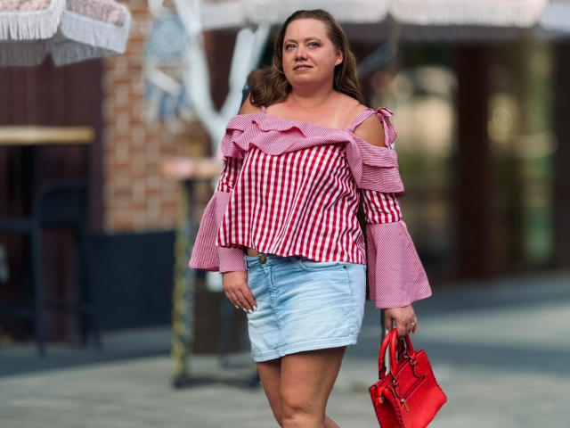 LillSandra with big tits, wearing a pink and red striped off-shoulder top, light blue denim skirt, and red handbag, walking confidently, holding her purse.