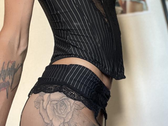 DaneeSoHot's black pinstriped lingerie, showing her ass, with lace panties and a detailed rose tattoo on her right butt cheek, standing in a slightly turned pose.