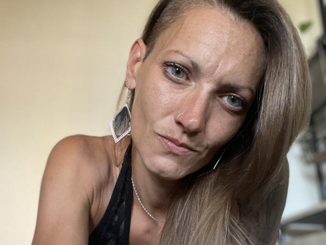 DaneeSoHot a un regard intense, avec des yeux bleus, un piercing au nez et de longs cheveux blonds. Elle porte de la dentelle noire et de grandes boucles d'argent, laissant apparaître ses épaules nues..
