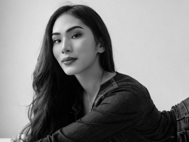 SofiaCumness with long dark hair, wearing a denim shirt, looking at the camera with a subtle smile, her boobs slightly visible, in a black-and-white portrait.