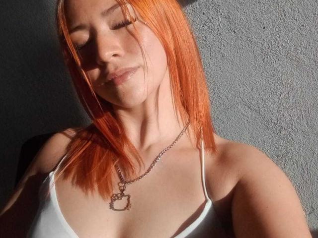 SamanthaCollen with orange hair, eyes closed, white spaghetti strap top, chain necklace with dog pendant, sunlight on her face, slight smile, soft shadows, relaxed pose.