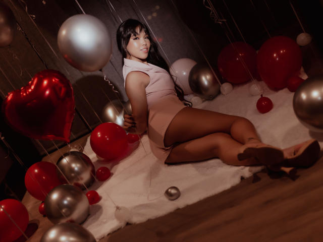 Heyly, met zwart haar en een bleke huid, ligt op een besneeuwde vloer, omringd door rode en zilveren ballonnen, sexy brunette in zwarte kousen, haar benen gespreid, terug te kijken naar de camera.