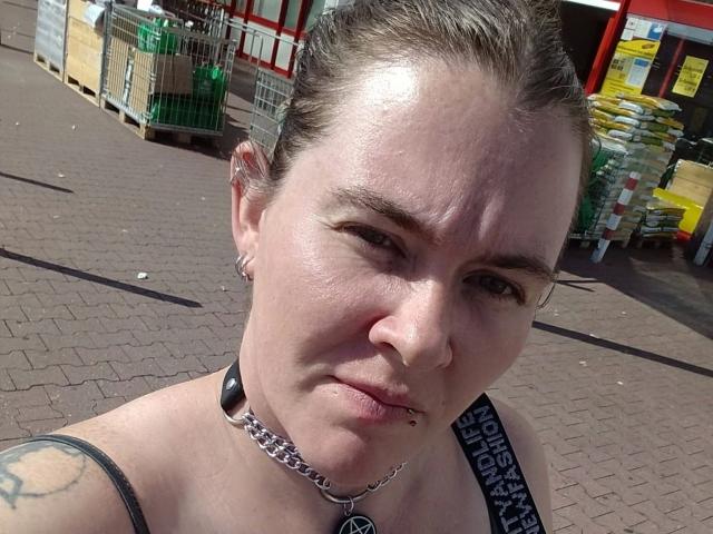 Rotkaeppchen-hot has a pierced nose, a chain necklace, and a tattoo on her shoulder. She's wearing a black top, with her hair pulled back. Her ass is not visible.