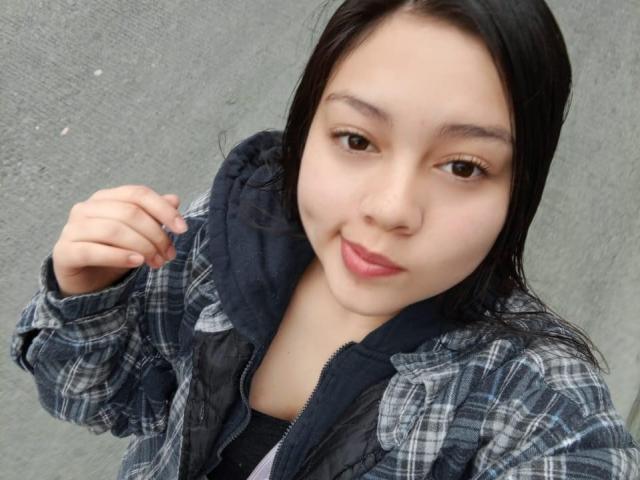 NatalliieSweet ha una carnagione media, capelli neri, occhi marroni e labbra rosa. Indossa una giacca a quadri sopra una felpa nera, sorridendo leggermente con una mano alzata..