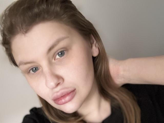 PassionFruitI has fair skin, blue eyes, and brown hair, with a hand in her hair, wearing a black top, and has pink, slightly glossy lips.