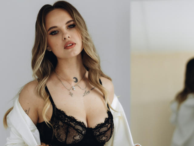 KhaleesiMoon with blonde wavy hair, wearing black lace bra, showing her big tits, white shirt off, silver necklaces, mirror reflection, soft light, sexy, seductive look.