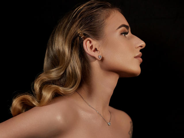 LaymaBlast's profile shot with wavy blonde hair, a small diamond earring, and a delicate necklace, showing off smooth, shiny skin and a subtle, confident expression.