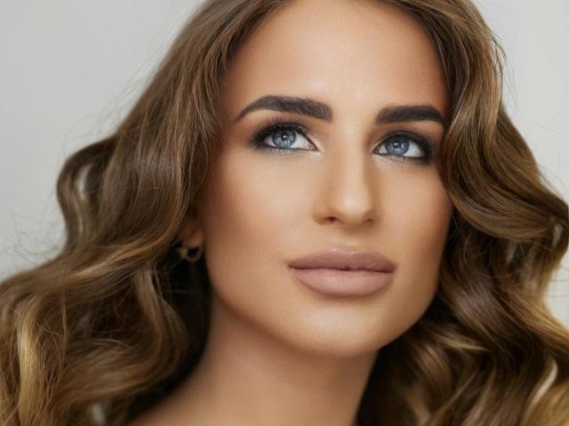 LaymaBlast has blue eyes, brown wavy hair, and a smooth, tan face with full lips and dark eyebrows. She looks confident and sexy.