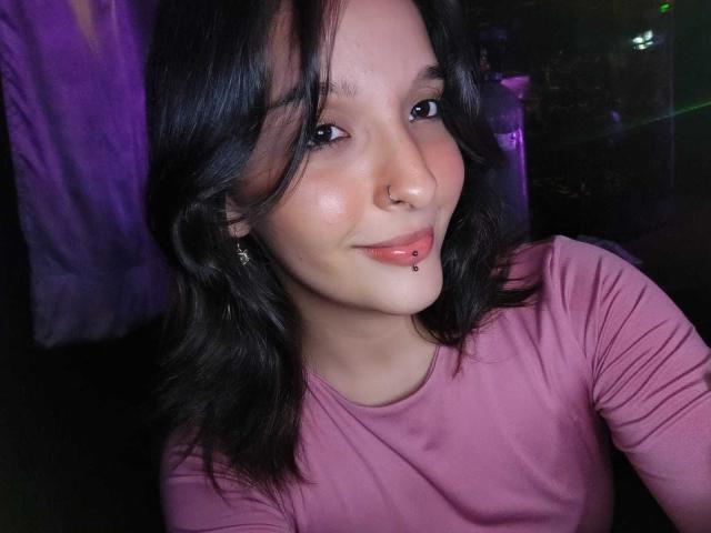 LanaKlaire ha capelli neri di lunghezza media, un piercing al naso e un piercing al labbro. Indossa una maglietta rosa, sta sorridendo e ha la pelle luminosa. Il suo seno non è visibile..