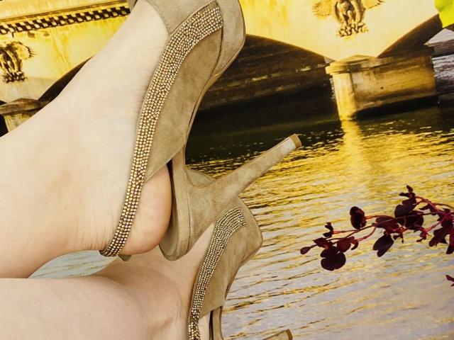 KarKutie's ass in suede high heels with gold studs, legs crossed, showing the sole of her foot. Red leaf in the lower right.