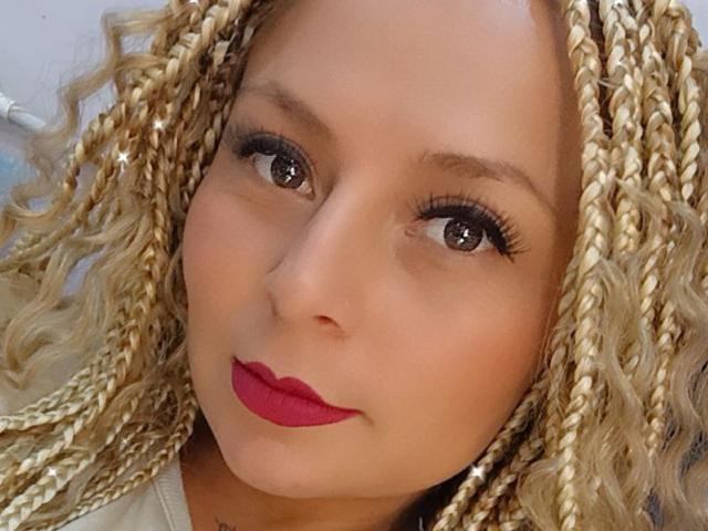 XimenaNahomi's face with blonde braids, brown eyes, red lipstick, and long eyelashes. She's got a cute, sexy look with her tits not visible in the image.