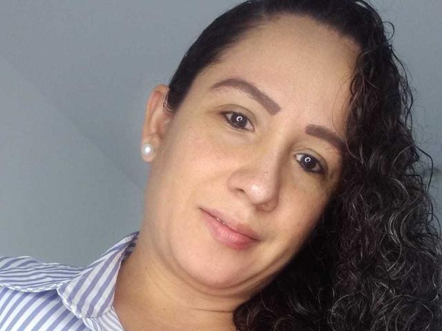BellaSmithHot has curly black hair, brown eyes, and wears pearl earrings. She's in a striped shirt with a slight smile, showing light freckles on her face.