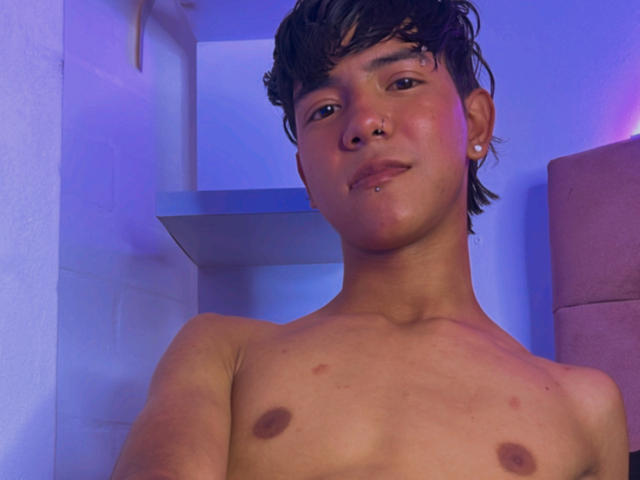 AresHearts, shirtless with small nipples, short brown hair, nose ring, and earring, smiling slightly, blue and purple lights in background.