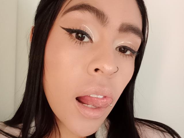 StellaBeckker's face, Asian woman with long black hair, ringed nose, glittery eyelids, sharp eyeliner, parted lips, tongue out, bottom lip piercing, white background, soft skin, sexy look.