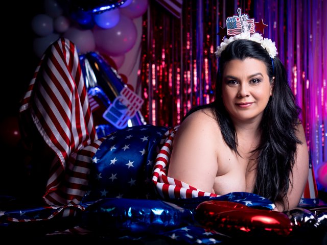 MartinaFox69 with big ass and tits, lying on American flag-themed balloons, wearing a star-spangled tiara, red and white striped gloves, and a blue star-patterned blanket.