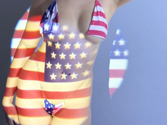AnastasiaEvansX in a bikini with American flag pattern, striped and star motifs, covering her tits and pussy. Shadow of flag on her, highlighting her curves and body.