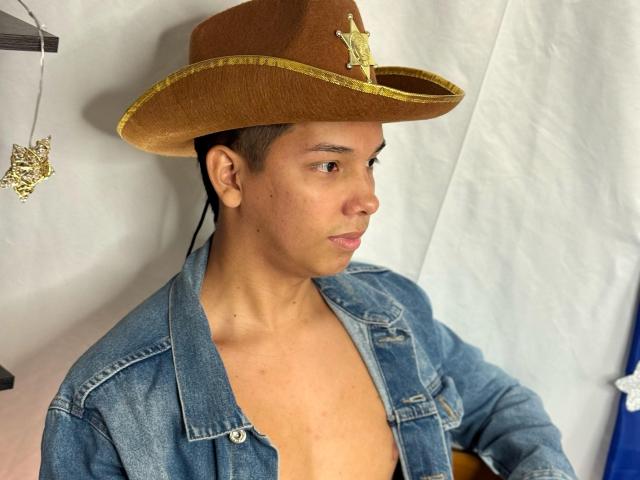 EdwinBlaze wearing a brown cowboy hat with a gold emblem, blue denim jacket, and no shirt, looking to the side with a neutral expression.