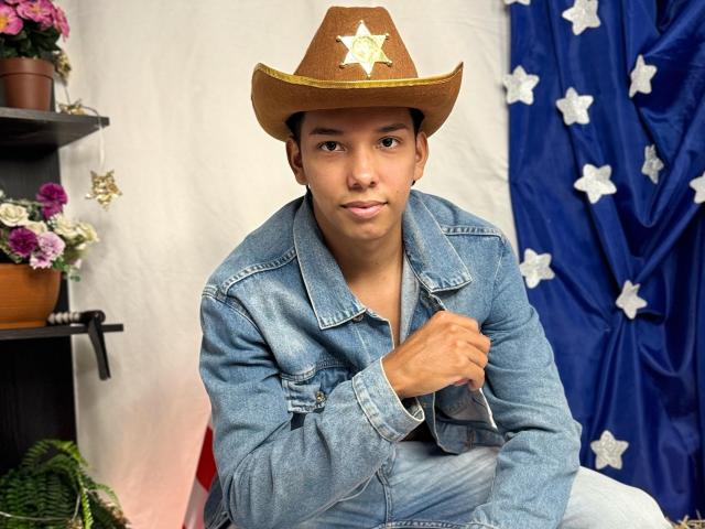 EdwinBlaze wearing a brown cowboy hat with a star, blue denim jacket, and holding a black wallet, sitting with a slightly confident, relaxed expression.