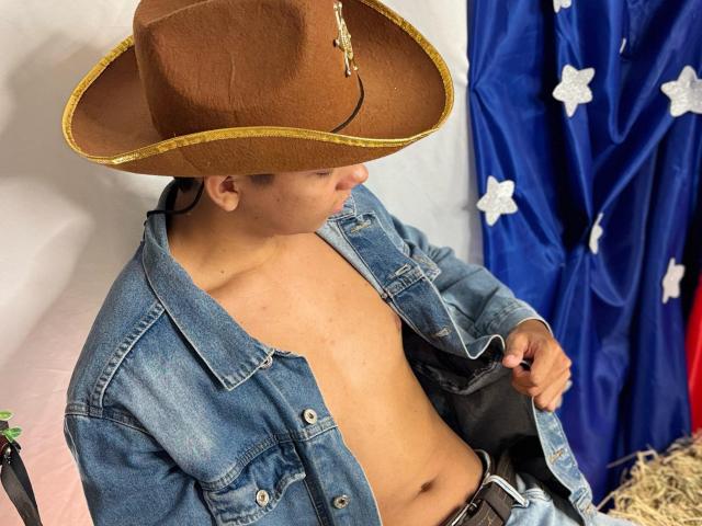 EdwinBlaze with a brown cowboy hat, blue denim jacket, and no shirt, showing his bare chest and slightly open jacket, holding a black object.