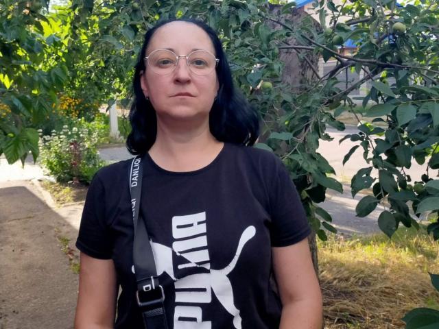 MelissaShell has blue-black hair, glasses, and wears a black Puma shirt with a white logo, standing outside with a gray strap bag. Her tits are average-sized.