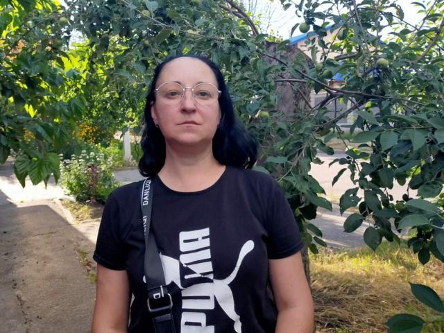 MelissaShell has black hair, glasses, and a serious expression. She's wearing a black Puma shirt with a white logo, and a gray strap is over her shoulder.