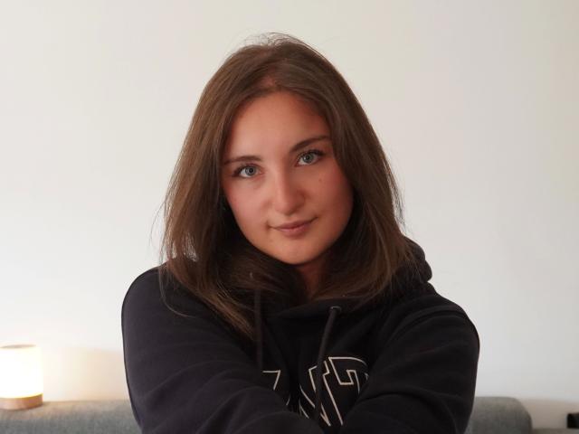 Evelynka-hot with medium brown hair, green eyes, and a slight smile, wearing a black hoodie, looking directly at the camera, soft natural light, casual indoor setting.
